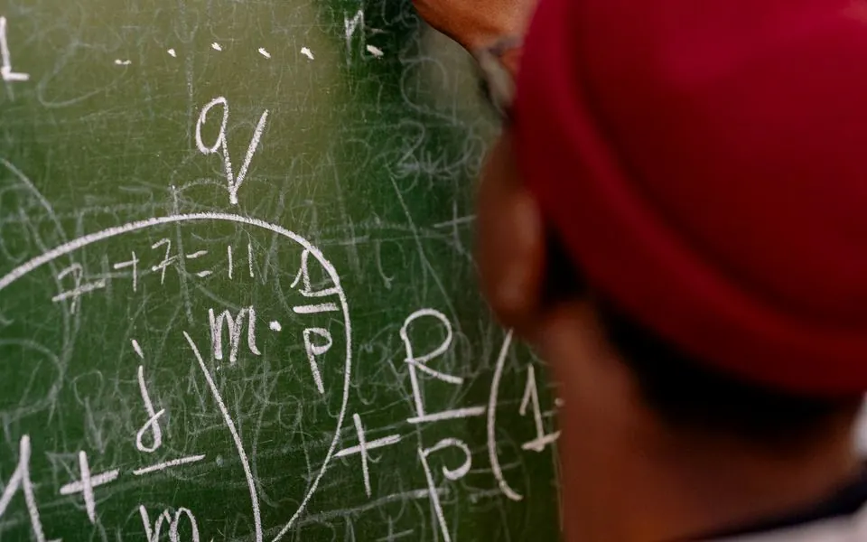 A learner’s hand and chalk against a blackboard.