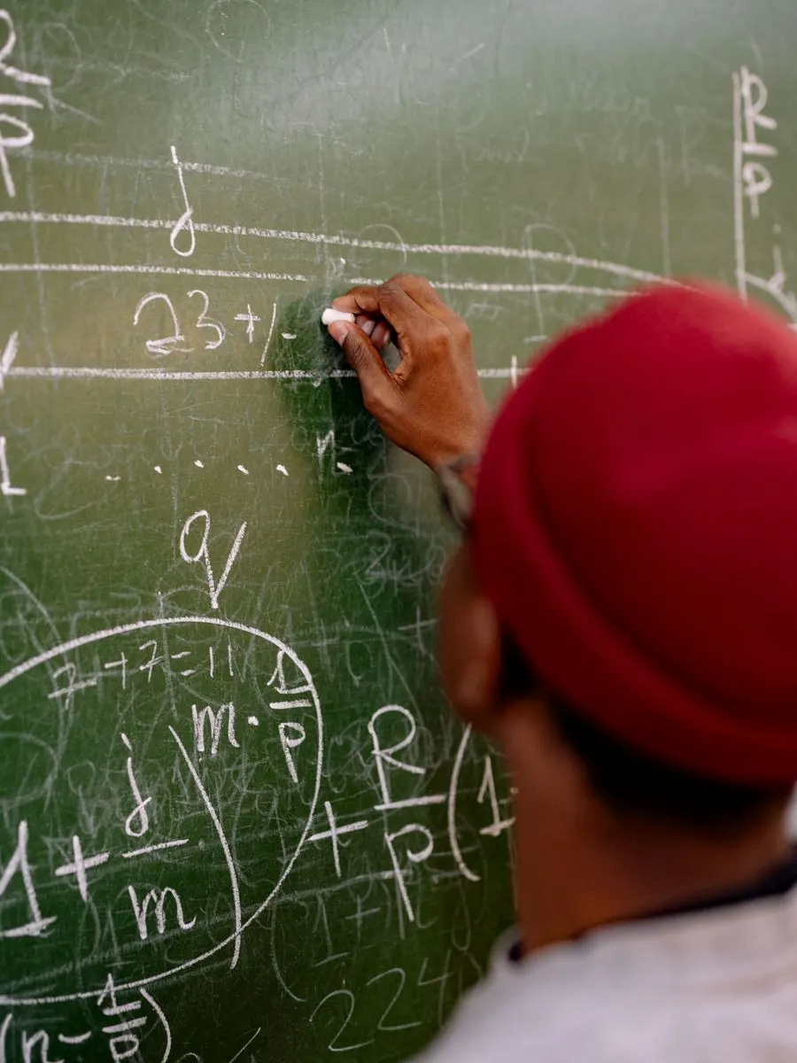 A learner writing an equation in chalk on a blackboard, seen from behind.