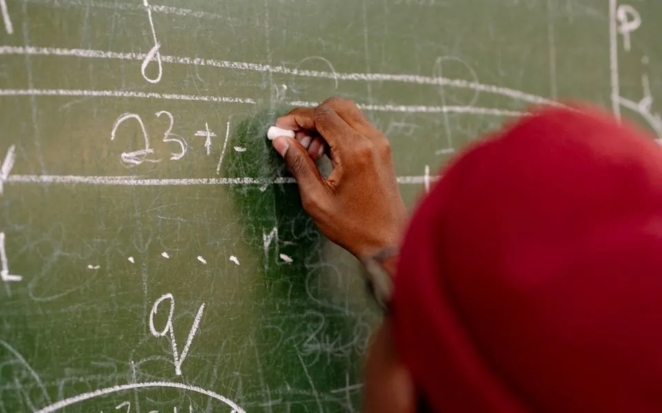 A hand writing an equation in chalk on a blackboard.