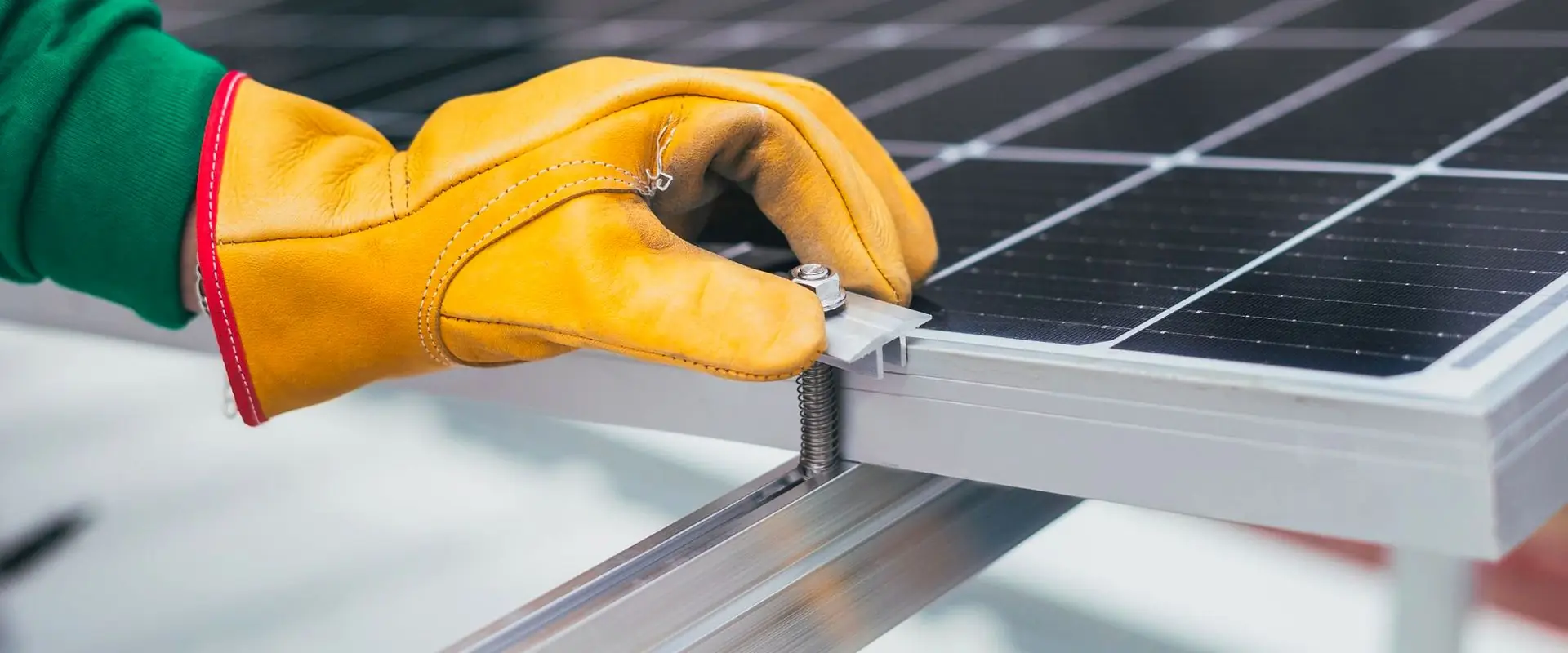 A gloved hand fitting a clamp to the frame of a solar panel.