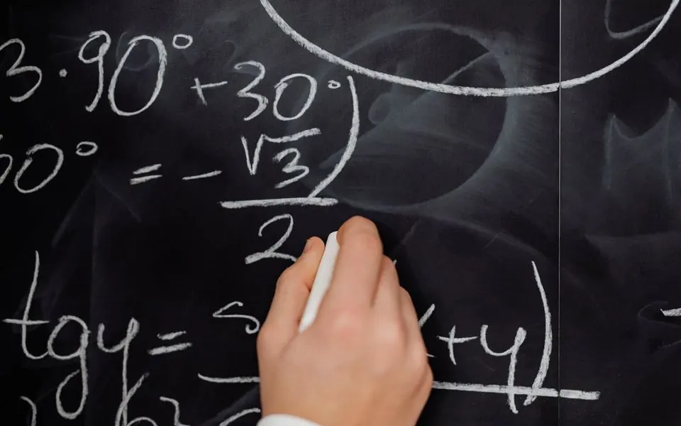 A hand writing a mathematical formula in chalk.
