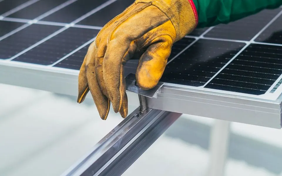 A gloved hand resting on a solar panel frame.