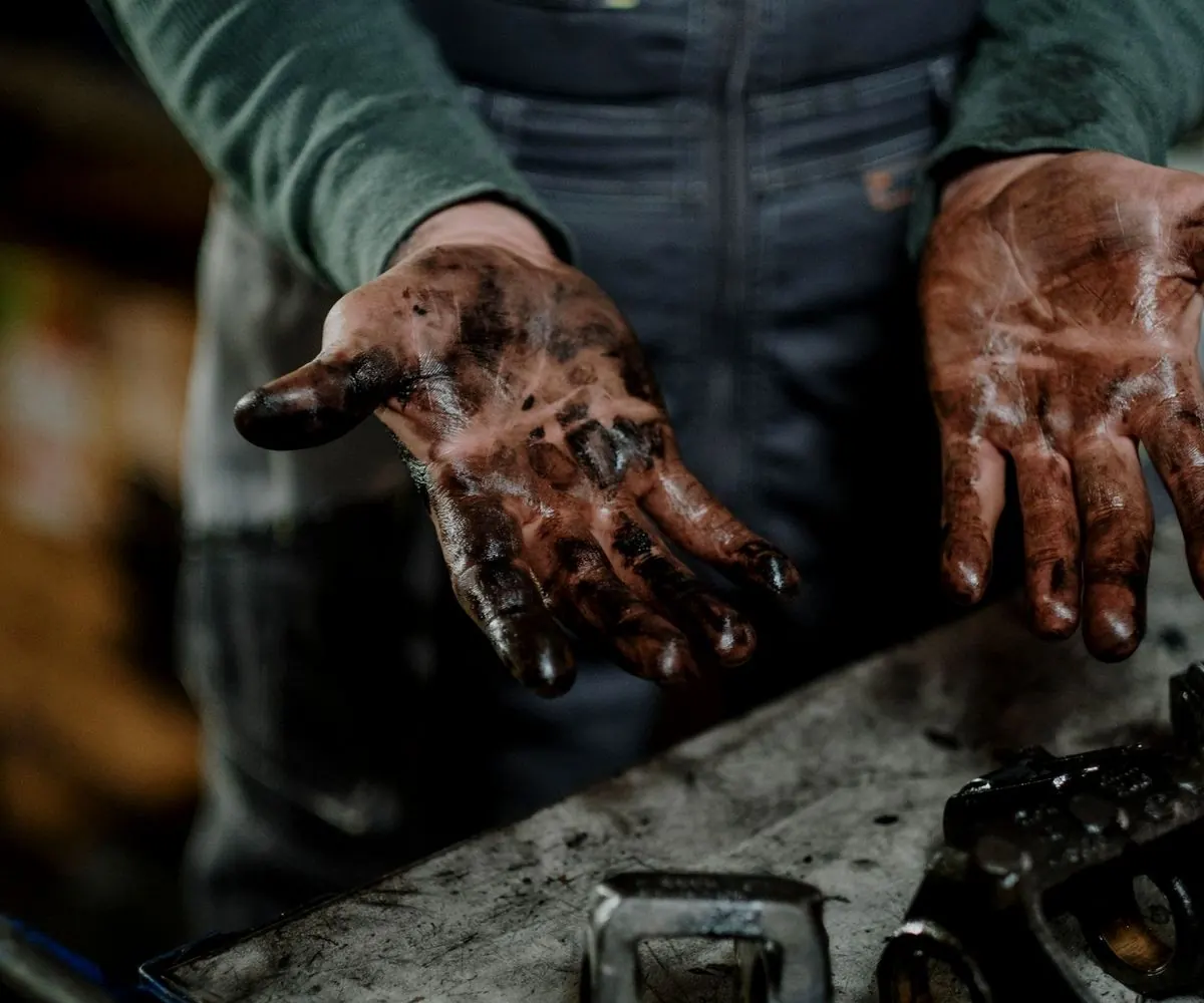 A pair of open hands, worked and oil-stained, held out over a bench.