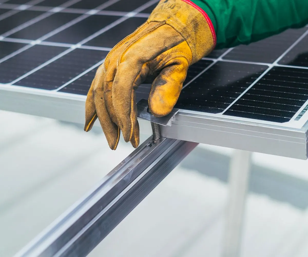 A gloved hand resting on the edge of a solar panel.
