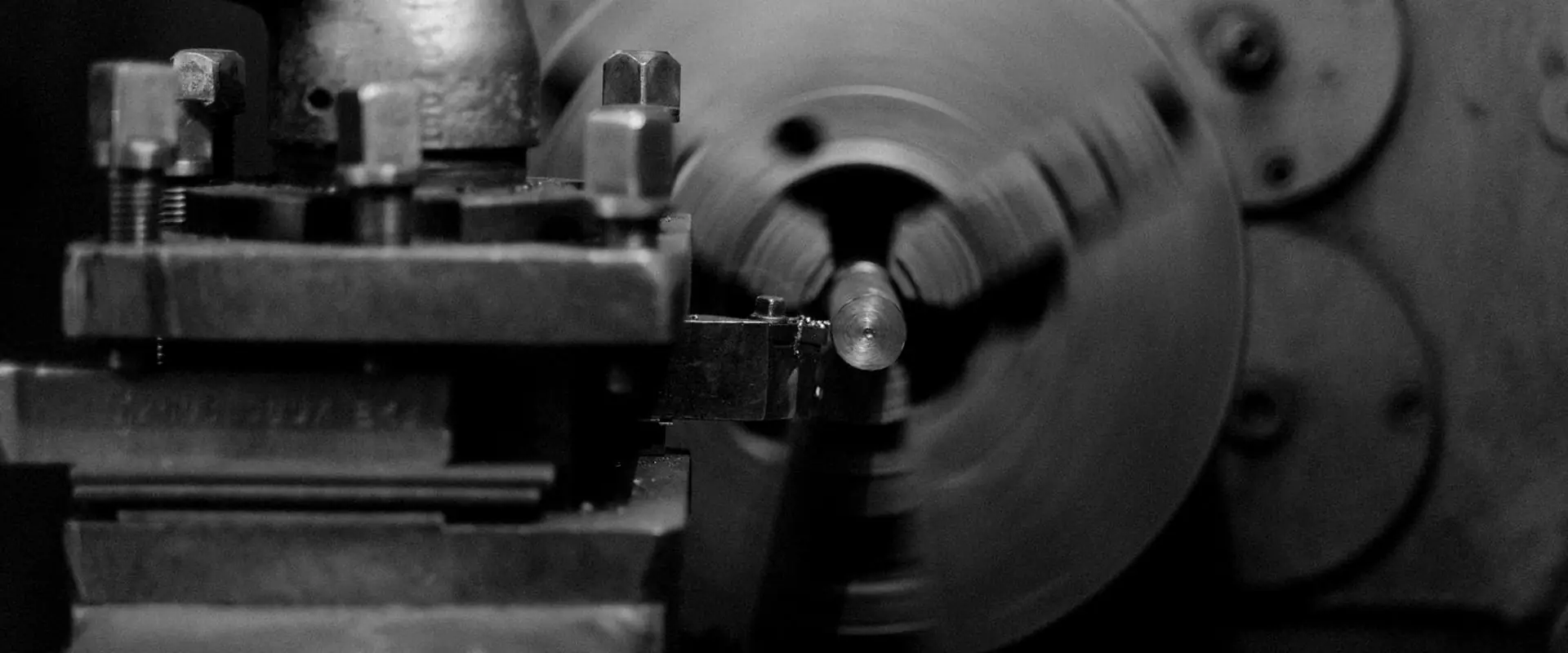 The head and chuck of a lathe, a part turning between the jaws.