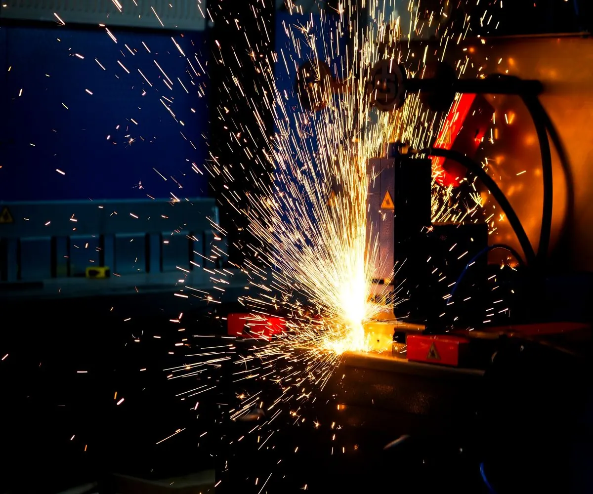 A burst of sparks thrown off a workpiece in a workshop, the machine around it in shadow.