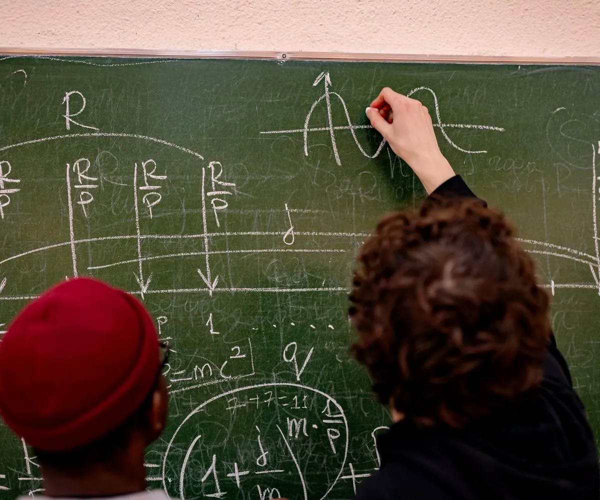 Two learners working at a blackboard, seen from behind.