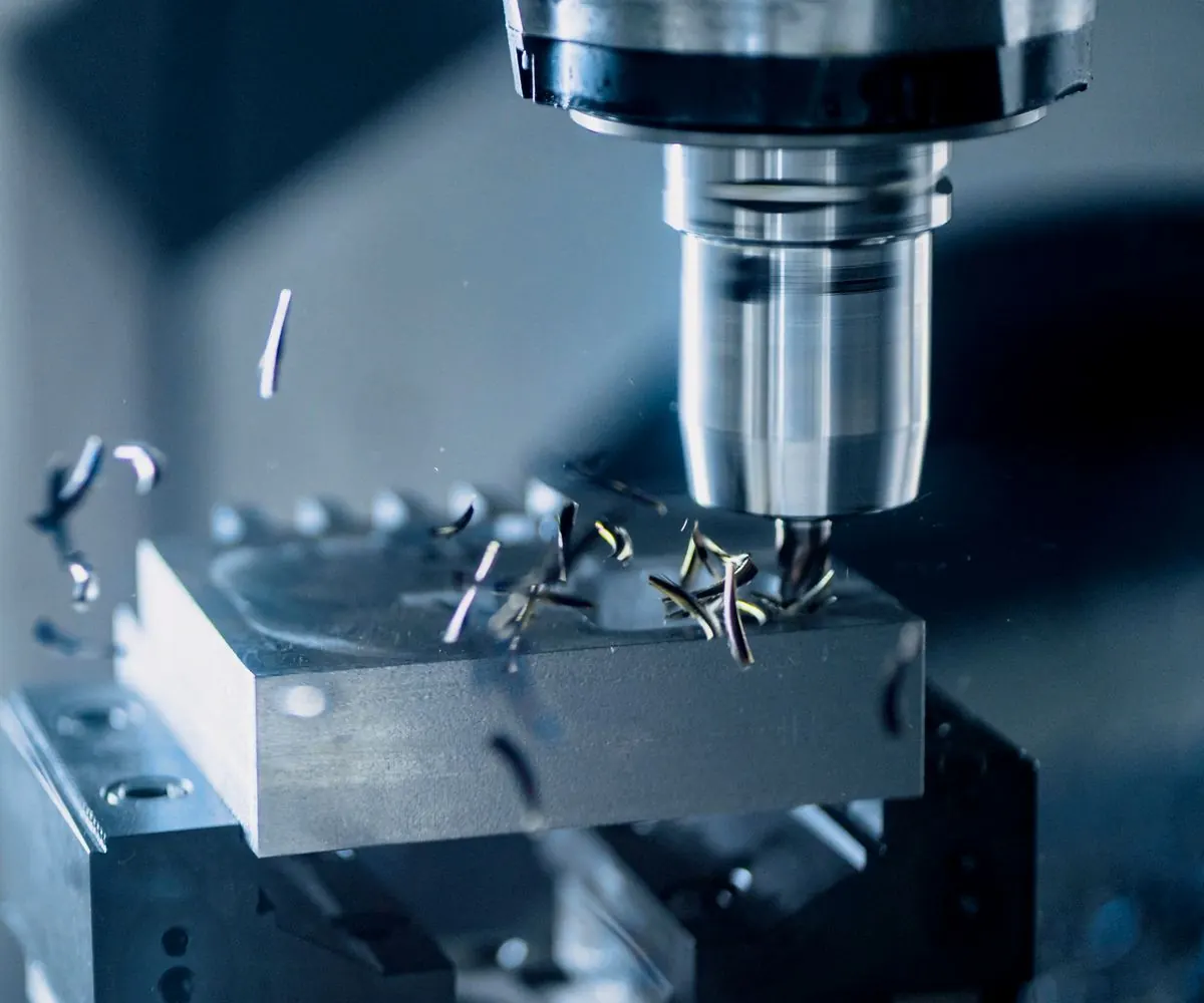 A CNC cutter working a metal block, swarf lifting away from the tool.